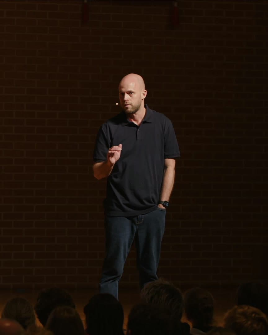 Mike Skinner speaking in low light against a brick wall